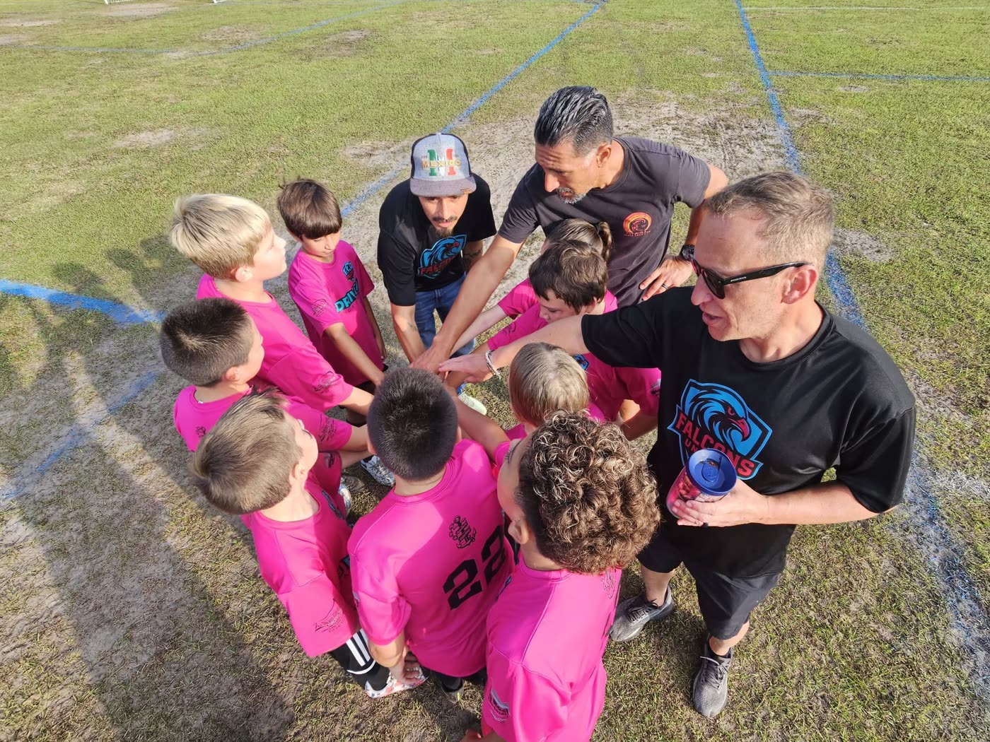 A Falcons United coach and young players in pink with their hands together in a team huddle