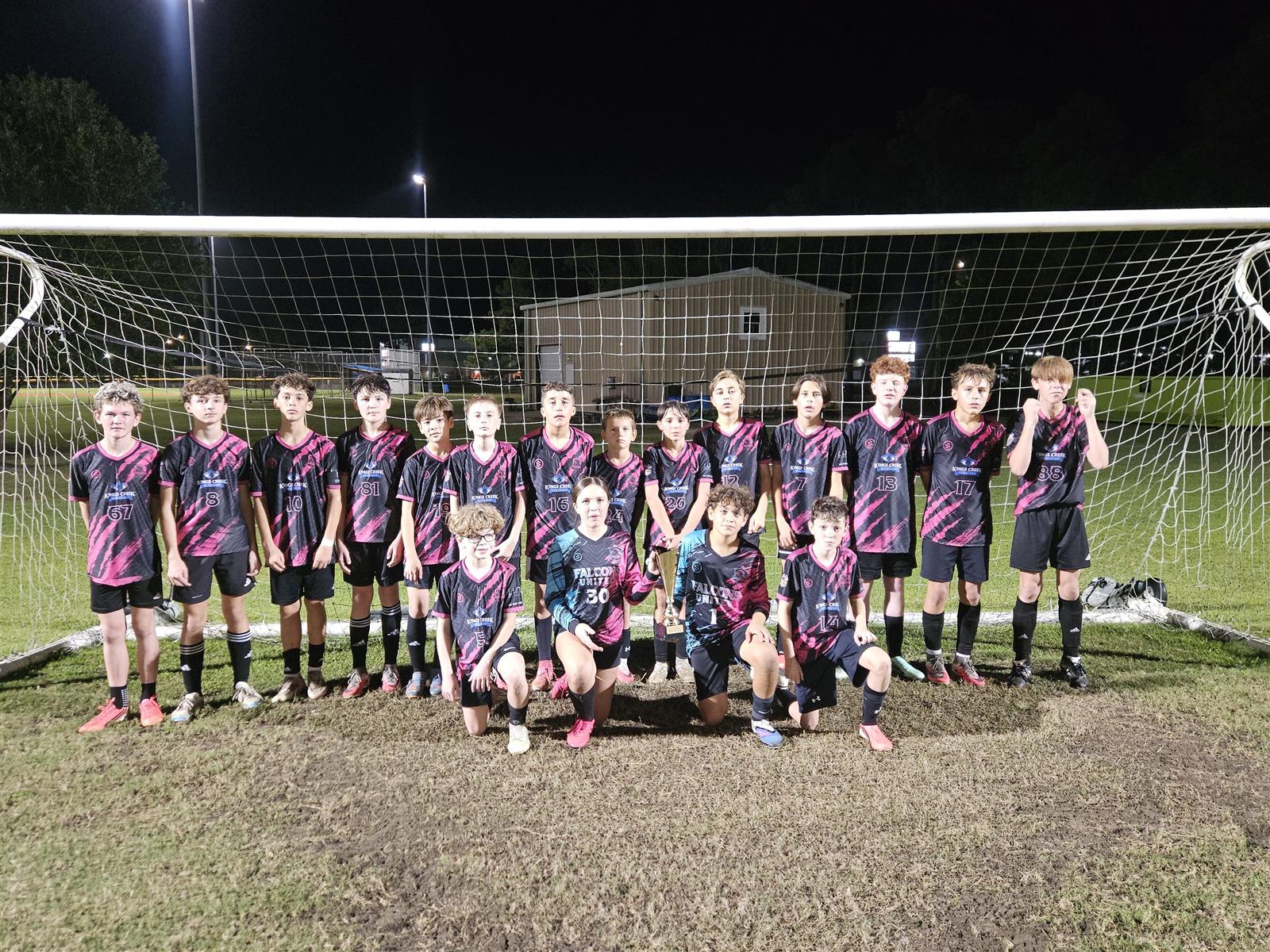 Falcons United team and goalkeepers posing in front of the goal with a trophy